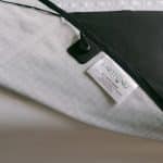 A close-up of a fabric product with a tag labeled Earthing®. The tag details the Earthing® Grounding Mattress Cover - Super King Size, which is attached to white and black grid-patterned material with a black cord and clip.